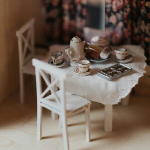 Charming miniature dollhouse dining room with an elegant tea set on a laced tablecloth.